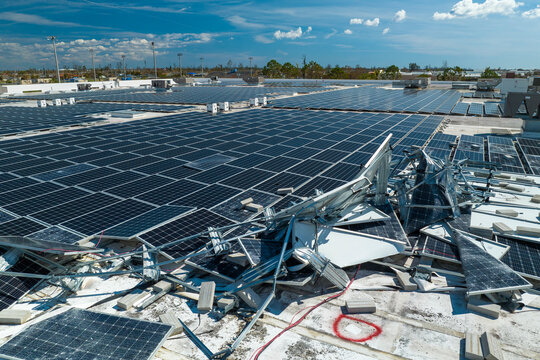 Broken down photovoltaic solar panels destroyed by hurricane Ian winds mounted on industrial building roof for producing green ecological electricity. Consequences of natural disaster