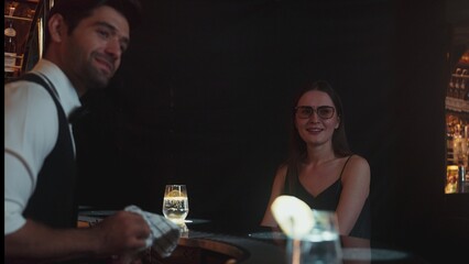 Focusing on beautiful woman guest sitting in special drink gin fizz at luxurious counter bar at vibrant nightlife party atmosphere. Smart bartender wiping glass while talking with customer. Vinosity.