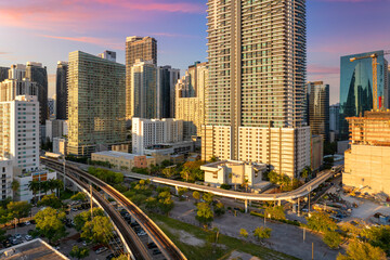 Public train system travels along elevated railroad in Miami downtown office district at sunset,...