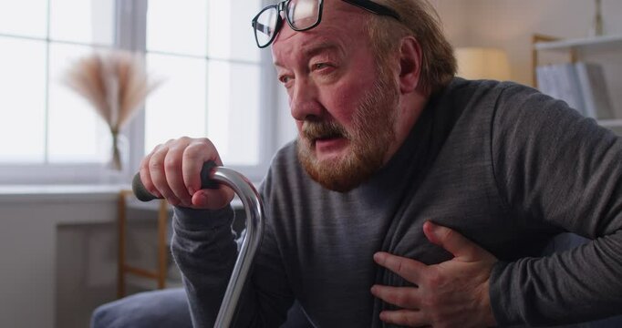 Senior man clutching chest, having heart attack, suffering from intense pain, needs painkillers to relieve pain, feeling discomfort, posing against home interior. Old people and health problems