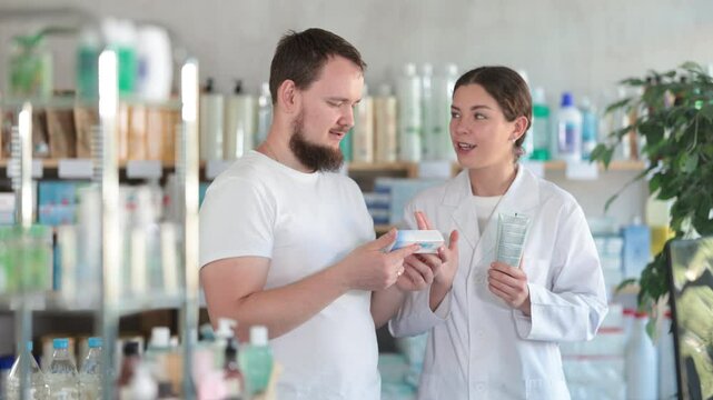 Man chooses ointment in modern pharmacy. Female pharmacist helps with choosing a medicine. High quality 4k footage