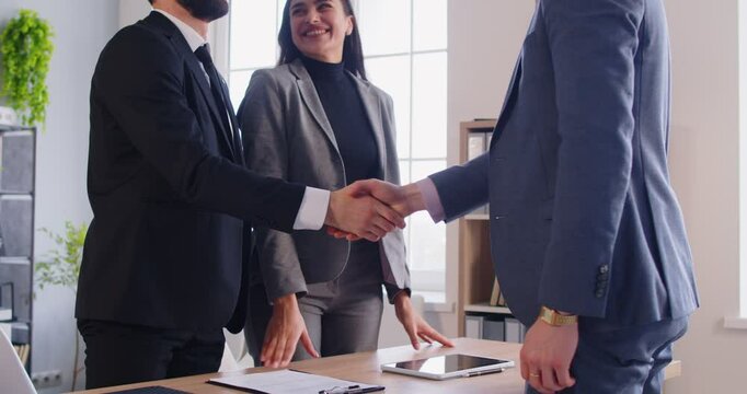 Smiling realtor shaking hands with young family couple, congratulating them with property purchase. Happy clients exchanging handshake with real estate agent after making successful deal in office.