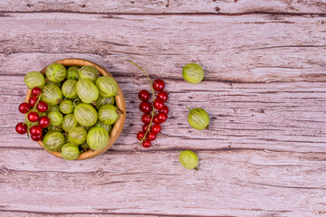 Fresh gooseberries and red currants in a wooden bowl and scattered on rustic wooden background....