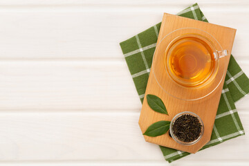 Cup of tea with dry and fresh leaves on wooden background, top view