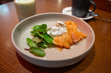 Poached egg with smoked salmon and avocado on a plate, served with fresh salad and a glass of smoothie for a healthy breakfast