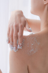 Female hands in a bright bathroom spreading blue cream on the body