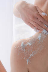 Fototapeta premium Female hands in a bright bathroom spreading blue cream on the body