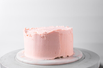 Pink buttercream cake on a cake plate, Cake covered in pink frosting, process of decorating a cake with pink buttercream