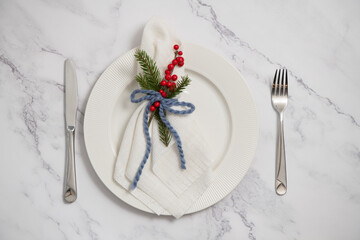 Festive christmas place setting with white plate, napkin, fir tree branch and red berries decoration on marble table