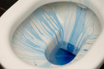 Blue toilet bowl cleaner drips down the sides of a white toilet bowl, showing its cleaning power