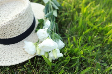 A stylish straw hat lies on vibrant, green grass, accompanied by a delicate bouquet of white...