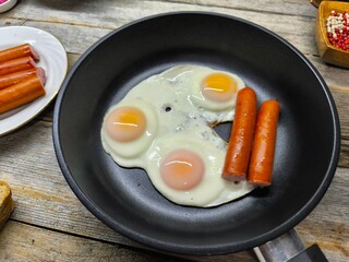 delicious appetizing breakfast of fried eggs and sausages on a frying pan