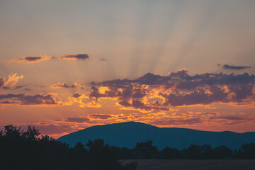 Vibrant sunset over rolling hills illuminating the sky with dramatic colors and shadows at dusk in a serene landscape