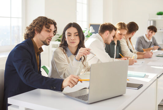 Portrait of young college or university students group sitting in the classroom looking at the laptop monitor screen working on educational project together. Education and knowledge concept.