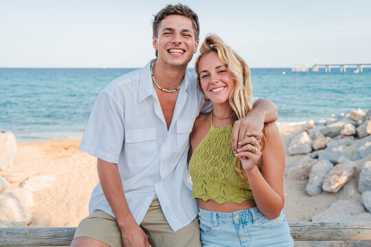 A joyful couple enjoys a sunny beach day together, smiling brightly as they pose for a cheerful photograph by the shore, capturing the essence of love and happiness during their memorable vacation.