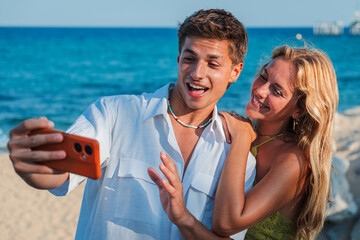 A cheerful couple enjoying their time at the beach while taking a delightful selfie with a...