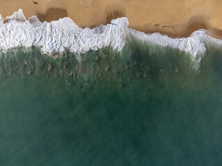 incredible view from above of the beach with blue water and waves forming