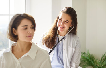 Smiling female doctor or nurse performing a medical checkup with a stethoscope to assess a patient...