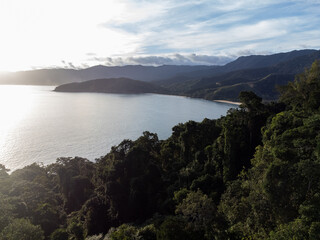 Setting sun on beautiful tropical beach amidst forested mountains
