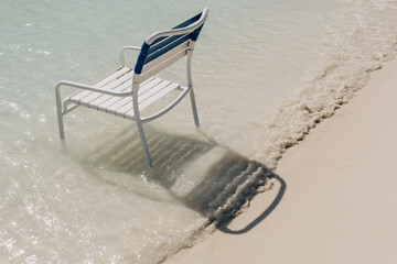 Chair resting near the shoreline as gentle waves lap at the sandy beach during bright daylight