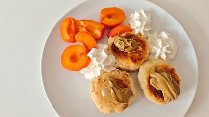 Cheese pancakes with peanut butter served with fresh apricots and whipped cream on a white plate