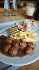 Swedish meatballs with gravy served with French fries and fresh salad on a white plate