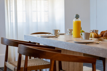 Petit déjeuner appétissant servi sur une élégante table en bois avec chaises en cannage, dans une salle lumineuse et chaleureuse.