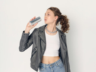 A stylish woman in fashionable clothes poses on a light background with a jar of energy drink in...