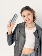 A stylish woman in fashionable clothes poses on a light background with a jar of energy drink in her hand