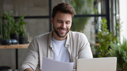 Smiling man looks pleased as he reviews important documents at a bright workspace filled with plants during daylight hours