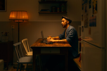 Caucasian man using laptop and cellphone sitting at home working in a kitchen home office.