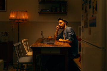 Caucasian man using laptop and cellphone sitting at home working in a kitchen home office.