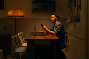 Caucasian man using laptop and cellphone sitting at home working in a kitchen home office.