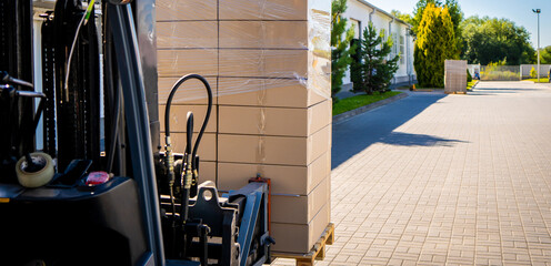 Forklift vehicle manipulating goods in logistic area outside warehouse.