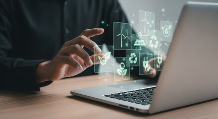 Person interacting with floating green energy icons on a laptop screen in a dark shirt setting