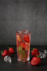 Refreshing drink with strawberries and ice on dark textured table against grey background