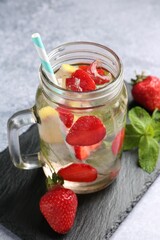Refreshing drink with strawberries, ice and mint on grey textured table, closeup