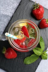 Refreshing drink with strawberries, lemon, ice and mint on grey textured table, top view