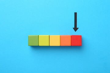 Maximum. Colorful cubes and arrow pointing at red one on light blue background, flat lay