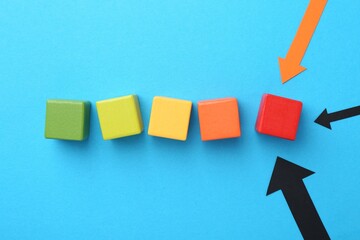 Maximum. Colorful cubes and arrows pointing at red one on light blue background, flat lay