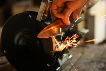 Man sharpening knife with bench grinder indoors, closeup