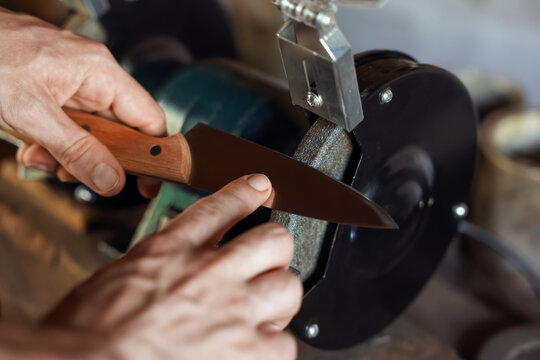 Man sharpening knife with bench grinder indoors, closeup