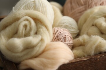 Soft felting wool and knitting yarn in wooden basket, closeup