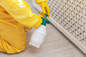 Pest control worker in protective suit spraying insecticide indoors, closeup