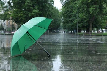 Green umbrella under heavy rain outdoors, space for text