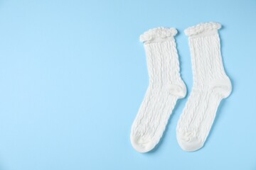 Pair of comfortable white socks on light blue background, top view. Space for text