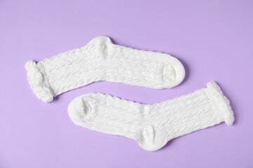 Pair of comfortable white socks on violet background, top view