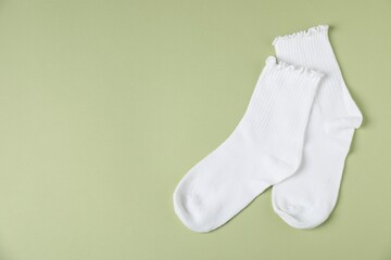 Pair of comfortable white socks on light green background, top view. Space for text