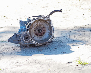Deserted and forgotten, a transmission sits on the sandy floor of a junkyard