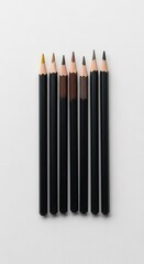 A row of sharpened colored pencils with black barrels on a white textured background